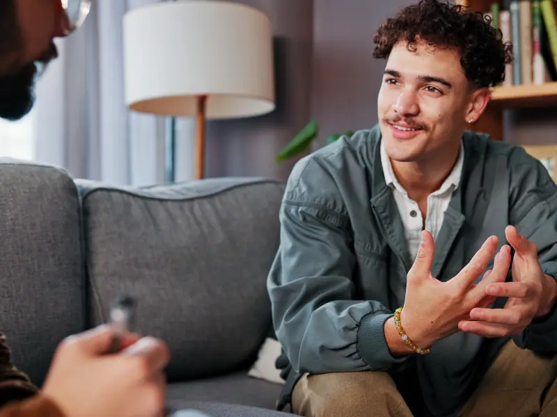 أخصائي علم النفس، معالج نفسي، ورجل سعيد يتحدثون لطلب المساعدة، أو للحصول على نصائح أو دعم في مجال الصحة النفسية في العيادة.